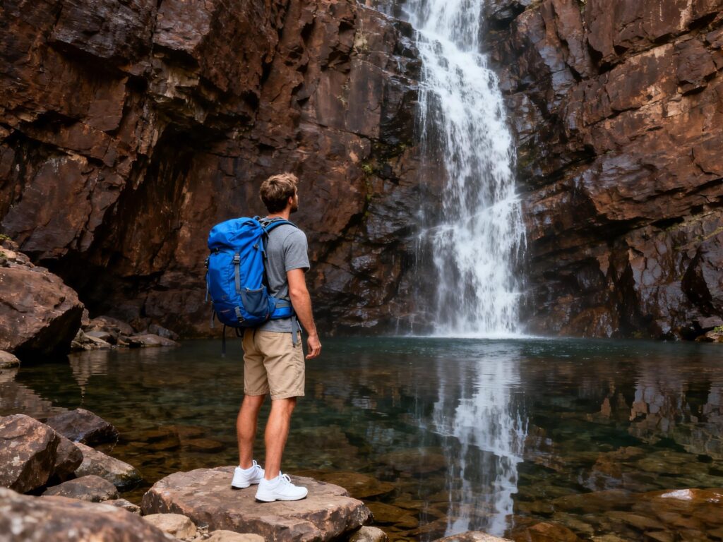 jimeng 2025 12 28 6213 摄影风格，一名外国男性徒步者站在岩石水潭边，背对镜头望向一个大型瀑布；他背着蓝色... 副本
